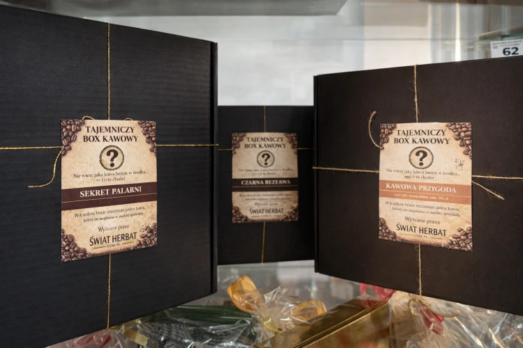 Realne zdjęcie pudełek w sklepie stacjonarnym - Tajemniczy box kawowy Świat Herbat – trzy zestawy prezentowe kawy w eleganckich czarnych pudełkach z etykietami Sekret Palarni, Czarna Rezerwa i Kawowa Przygoda
