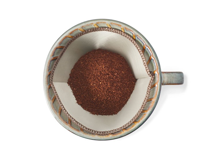 Widok z góry na stalowy filtr Elian umieszczony w filiżance z mieloną kawą – przykład użycia podczas parzenia metodą pour-over.